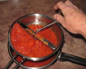 Photo of tomatoes being pushed through a mouli sieve.
